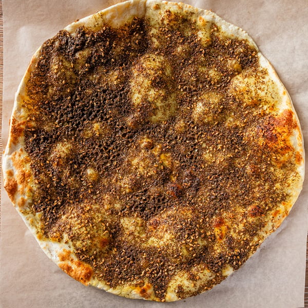 Zazzy's Lebanese za'atar manoushe, a flatbread topped with herbs and sesame seeds, on parchment paper.