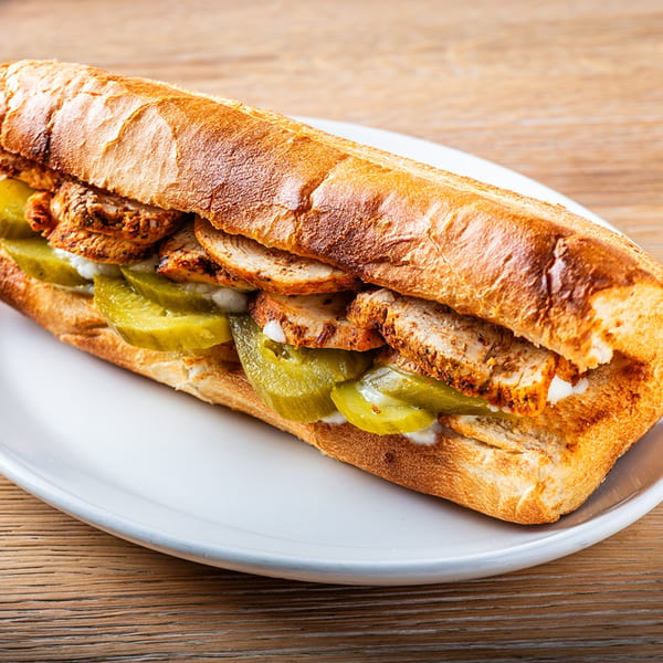 Zazzy's Lebanese chicken shawarma sandwich with pickles and garlic sauce on a white plate.