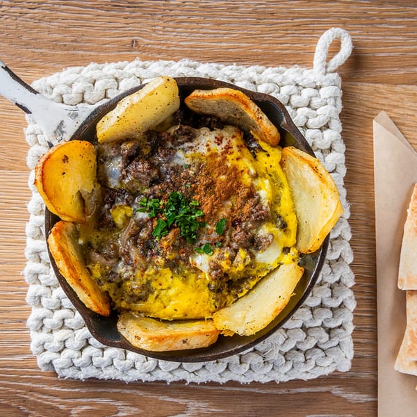 Lebanese baked eggs with spiced ground meat, potatoes, and fresh herbs in a skillet.