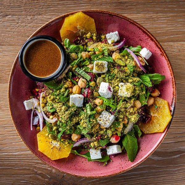 A vibrant Lebanese salad with chickpeas, feta, mint, pistachios, and orange slices, served with dressing.