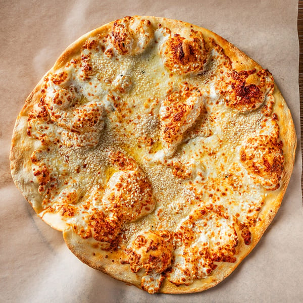 A close-up, overhead view of a Zazzy Lebanese cheese manakish with sesame seeds on parchment paper.