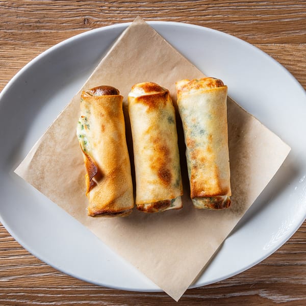 Three golden-brown Lebanese spring rolls, likely filled with cheese, on a white plate with brown parchment paper.